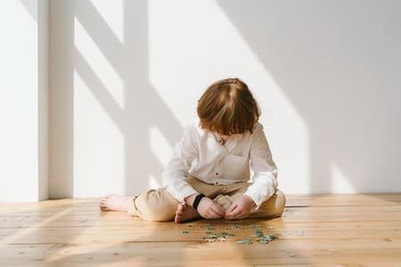 Foto de umca criança ruiva de cabelo liso, sentado no chão, de cabeça baixa, com peças de quebra-cabeça, com comportamento parecido do autismo, ou de uma criança autista. A foto ilustra o artigo "Donald Winnicott e a teoria sobre o objeto transicional" escrito pelo psicanalista Homero Monaco para o blog do site Online Psicanalista.