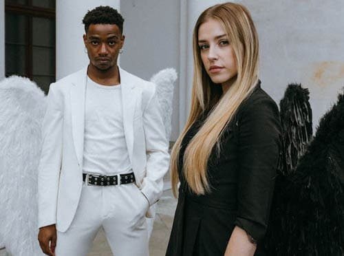 Foto de homem preto, com calça, camisa e blazer brancos e com asas brancas. Nela também aparece uma mulher com cabelo loiro longo, vestida de preto e com asas pretas. A foto ilustra o tópico Id, ego e superedo do artigo de Homero Mônaco do blog do site Online Psicanalista.