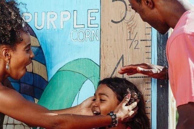 Foto de pais pretos medindo a altura do o filho em uma régua gigante. A imagem ilustra o artigo Revelando os Segredos do crescimento pessoal do blog do Homero Mônaco para o Site Online Psicanalista.