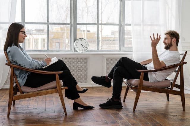 Foto onde aparecem duas cadeiras, uma em frente a outra. Em uma delas uma mulher com folhas na mão, e na outra um homem gesticulando e falando. A foto ilustra o artigo "Quais são as diferenças entre psicanalista e psicólogo?" escrito pelo psicanalista Homero Mônaco para o blog Online Psicanalista.