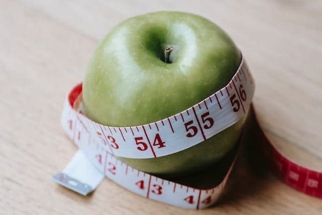 Foto de uma maça verde, com um fita métrica em volta. A foto ilustra o artigo"Transtornos Alimentares: O Impacto do Cérebro na Imagem Corporal" escrito no blog do psicanalista Homero Mônaco para ao site Online Psicanalista.