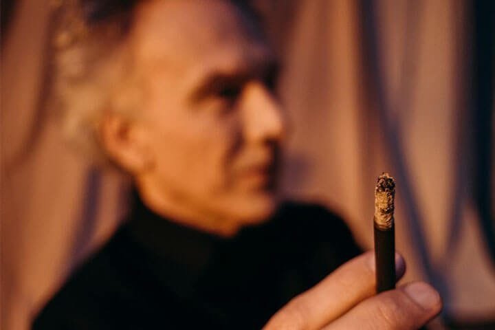 Foto de um homem de perfil, sentado e em primeiro plano está a mão dele com uma cigarrilha na mão. A foto ilustra o artigo 7 maneiras de como a psicanálise vai te ajudar no tratamento da dependência escrito no blog do psicanalista Homero Mônaco para ao site Online Psicanalista.
