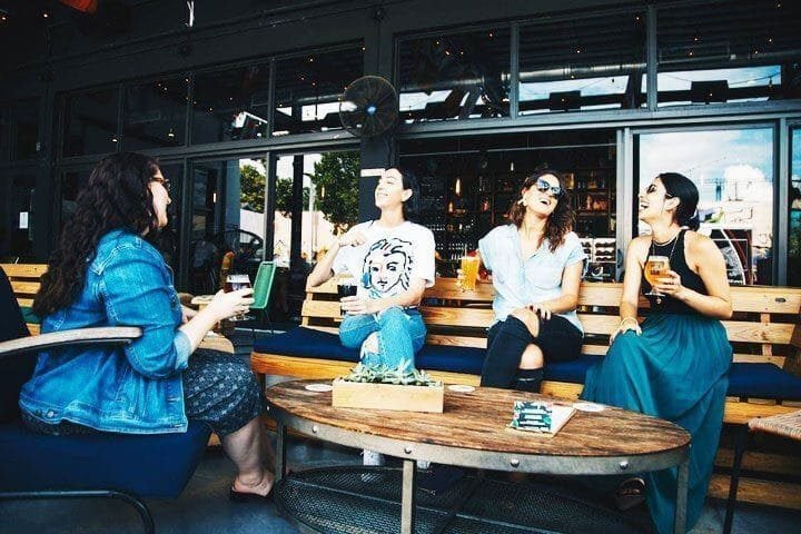 Foto de 4 amigas sentadas em uma banco de madeira, em frente a um restaurante, conversando e rido fortalecendo a relação de amizade entre elas. A foto ilustra o artigo 10 Melhores Maneiras para Construir a Resiliência Emocional com a Psicanálise escrito pelo psicanalista Homero Mônaco para o site Online Psicanalista.