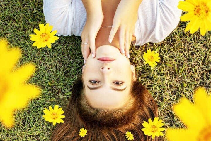 Foto de uma mulher deitada na grama, rodeada de flores amarela, e acariciando o próprio rosto. A foto ilustra o artigo 10 Passos para Alcançar Equilíbrio Emocional Através da Psicanálise escrito pelo psicanalista Homero Mônaco para o site Online Psicanalista.