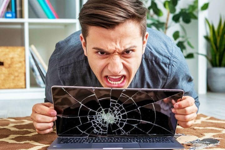 Foto de um homem atrás da tela de um notebook com a tela quebrada. O homem está com cara de raiva. A foto ilustra o artigo 5 Dicas Confiáveis para Reconhecer Padrões Destrutivos escrito pelo psicanalista Homero Mônaco para o site Online Psicanalista.