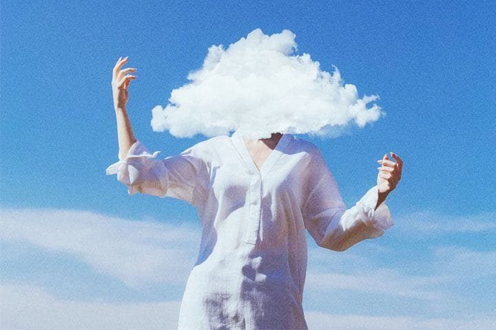 Foto de um mulher de frente, com um fundo de céu azul com nuvens brancas. Em cima do rosto dela está uma nuvem branca, fazendo referência ao inconsciente. A foto ilustra o artigo Aproveitando o Poder da Mente Inconsciente escrito pelo psicanalista Homero Mônaco para o site Online Psicanalista.