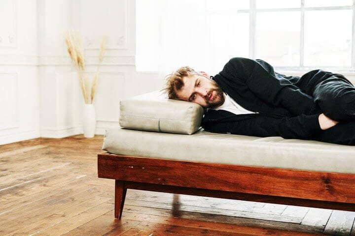 Foto de um homem deitado de lado em um divã de psicanalista em posição fetal. Ele parece estar com depressão. A foto ilustra o artigo Como a Psicanálise trata a depressão escrito no blog do psicanalista Homero Mônaco para o site A Sessão de Terapia.