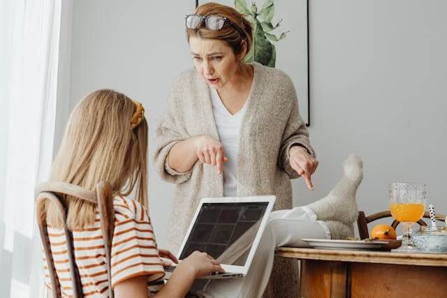 Foto de uma mãe chamando a atenção da filha pois ela está sentada em uma cadeira, com computador no colo e os pés em cima da mesa de jantar cheia de comida. A foto ilustra o artigo Compreenda 80% das suas motivações ocultas por trás das suas ações escrito pelo psicanalista Homero Mônaco para o site Online Psicanalista.