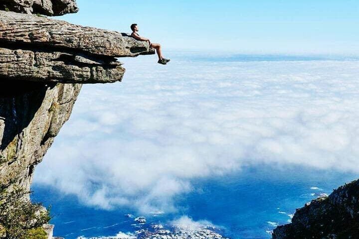 Foto de um homem sentado em uma pedra suspensa de um penhasco. A foto ilustra o artigo Explorando os Impulsos do Comportamento Humano escrito pelo psicanalista Homero Mônaco para o site A Sessão de Terapia.