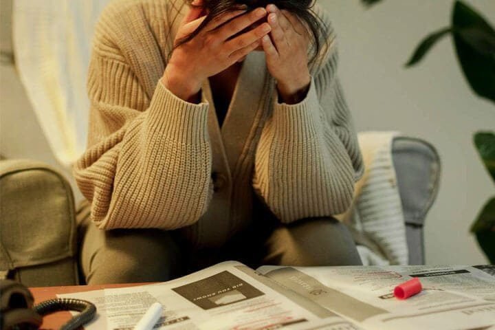 Foto de uma mulher com mão no rosto, e cabeça abaixada, debruçada em um jornal como se estivesse preocupada com a sua busca de emprego. A foto ilustra o artigo Os Impactos Causados pela Inteligência Artificial: Social, Comportamental, Psicológico e Cognitivo escrito pelo psicanalista Homero Mônaco para o site Online Psicanalista.