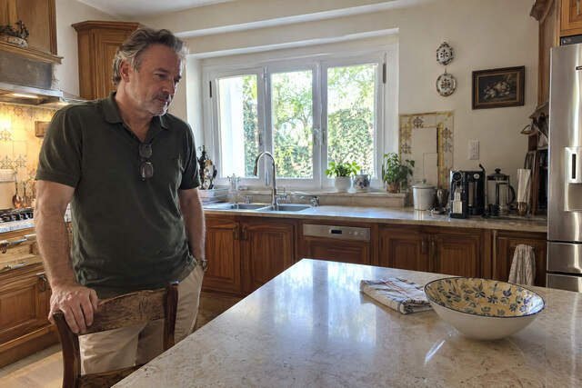 Homem de cerca de 49 anos em pé na cozinha antiga da casa onde passou a infância, com uma das mãos apoiada no encosto de uma cadeira de madeira gasta. Ele observa a mesa simples diante de si, cercada por azulejos antigos, com expressão distante e reflexiva. A cena remete às lembranças da infância e à influência das experiências passadas sobre o comportamento adulto. Imagem utilizada para ilustrar o artigo “75% do seu Comportamento foi Moldado pelas Experiências da sua Infância” escrito por Homero Mônaco Psicanalista especializado em neurociências e comportamento.