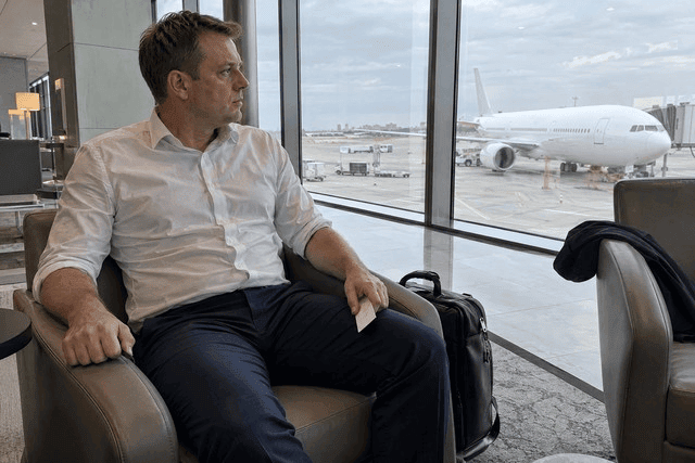 Homem sentado no saguão de um aeroporto, olhando pela janela para um avião, com a mão apertando o braço da poltrona. A postura rígida e a expressão apreensiva sugerem desconforto diante da perspectiva de viajar. O cartão de embarque permanece virado para baixo, sem informações legíveis, enquanto a janela e o avião contextualizam a situação que desperta receio. Imagem utilizada para ilustrar o artigo “Por que a psicanálise oferece ajuda genuína para fobias?” escrito por Homero Mônaco Psicanalista especializado em neurociências e comportamento.